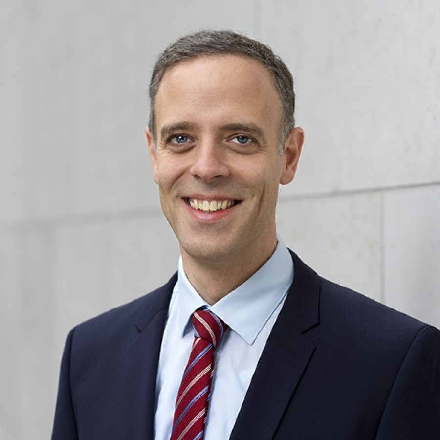 Dr. Markus Richter in Anzug mit Krawatte, vor einer hellen Wand, mit freundlichem Lächeln